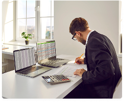 Bookkeeper tracking business expenses on two laptops with a calculator