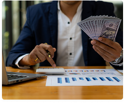 Accountant counting cash while recording income beside a laptop